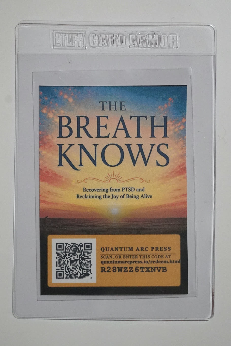 Tarjeta enfundada de The Breath Knows. Una portada con un amanecer y el subtítulo Recovering from PTSD and Reclaiming the Joy of Being Alive, sobre un cuadro QR y un código.
