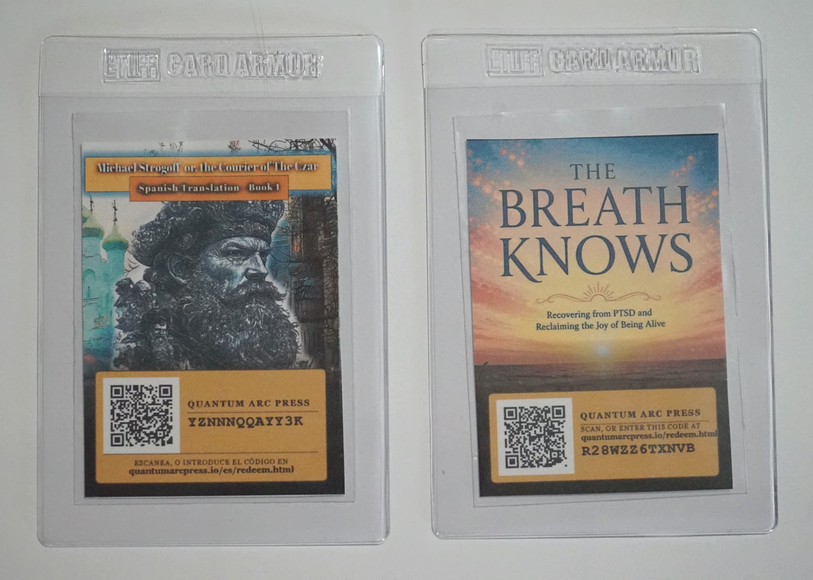 Dos tarjetas enfundadas de Quantum Arc Press una al lado de la otra. A la izquierda la edición en español de Miguel Strogoff, a la derecha la edición en inglés de The Breath Knows.